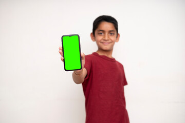 Young Indian Kid holding a phone in his hands with a green screen standing on a white isolated background with copy space.