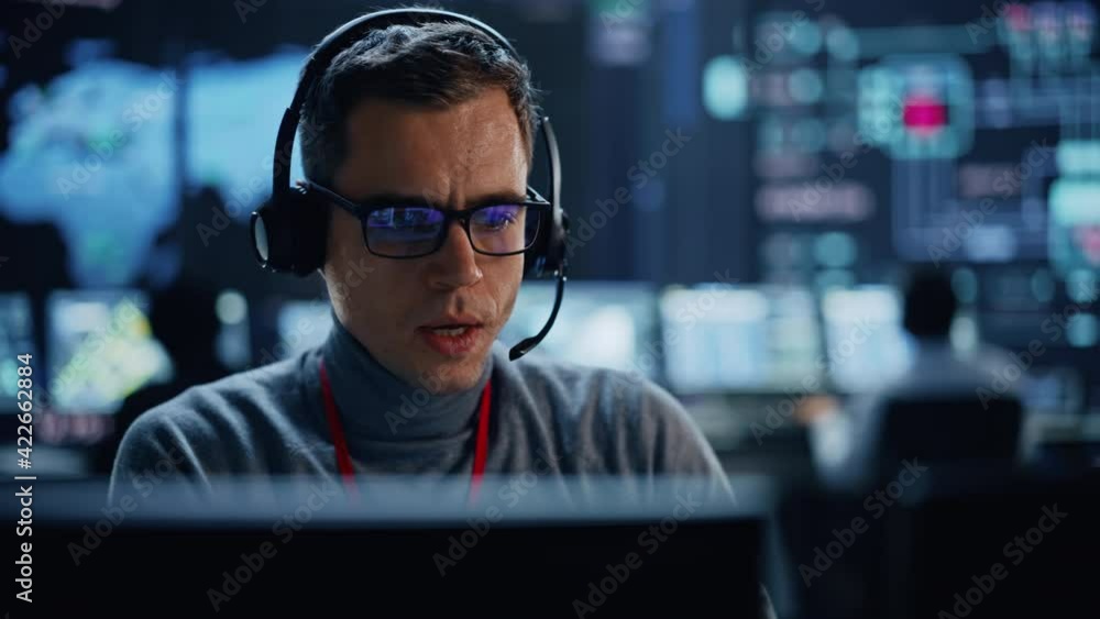 Aufkleber Portrait of Professional IT Technical Support Specialist Working on Computer in Monitoring Control Room with Digital Screens. Employee Wears Headphones with Mic and Talking on a Call.