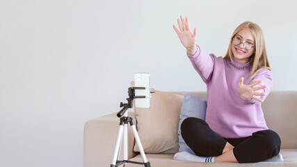 Young attractive woman greeting followers. Blogger or vlogger recording video on mobile phone at home and making content for internet isolation concept.