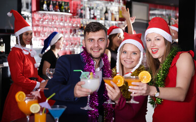 Cheerful guy with two girls funning and toasting drinks on new year eve party in bar