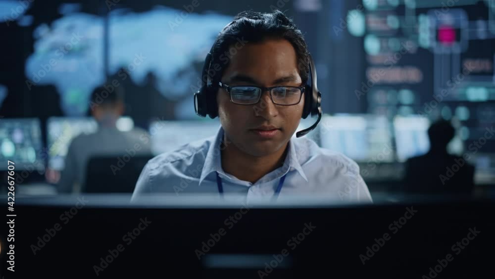 Aufkleber Portrait of Professional IT Technical Support Specialist Working on Computer in Monitoring Control Room with Digital Screens. Employee Wears Headphones with Mic and Talking on a Call.