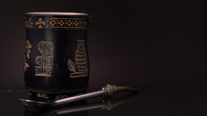 Mate negro grabado con bombilla plateada y fondo negro.