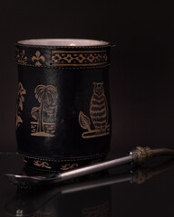 Mate negro grabado con bombilla plateada y fondo negro.