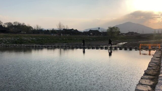 People crossing the stone bridge of a sunset stream in Gyeongju.