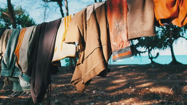 Clothes are dried on a rope in a poor African village. Various Colourful clothes, T-shirts, pants hanging out to dry on a clothesline between the palm trees. Lot of Washings are drying outside. Africa