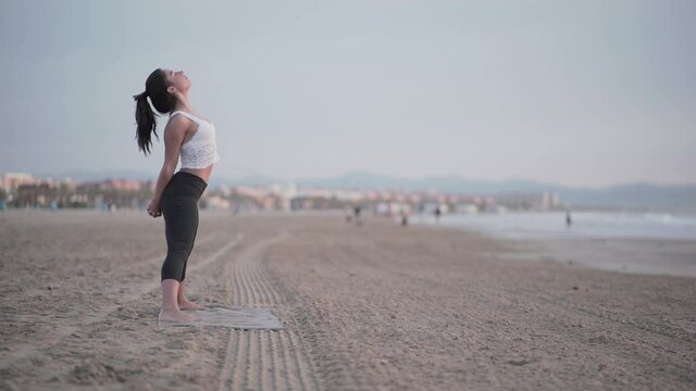 Prasarita Padottanasana - Girl On Beach Practicing Yoga And Doing Wide-legged Standing Forward Bend Pose On Mat. - wide shot
