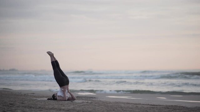 Yogi Showing Sarvangasana Pose (Shoulder Stand Pose) At The Coast On A Sunset. Yoga Meditation And Spirituality At The Beach In Valencia, Spain - wide shot