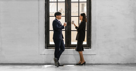 business partner holding coffee cup on hand standing by office window together having business discussion