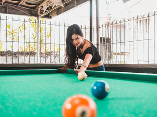 A pretty asian lady playing a game of billiards aiming for the number 2 ball. At an open air and...