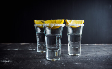 Silver tequila in shots with lemon slices on the dark rustic background. Selective focus. Shallow...