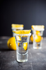 Silver tequila in shots with lemon slices on the dark rustic background. Selective focus. Shallow depth of field.