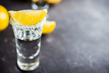 Silver tequila in shots with lemon slices on the dark rustic background. Selective focus. Shallow...