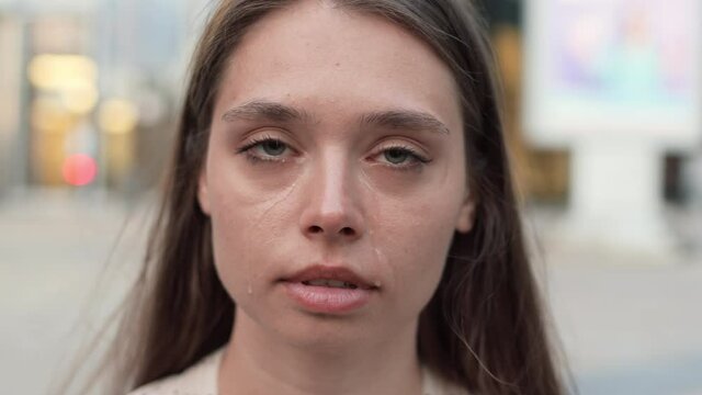 Close-up POV of young upset Caucasian woman crying, wiping off tears, looking on camera on blurred background