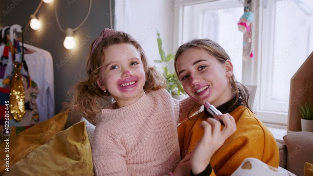 Wall mural Sisters indoors at home, applying lipstick. Lockdown concept.