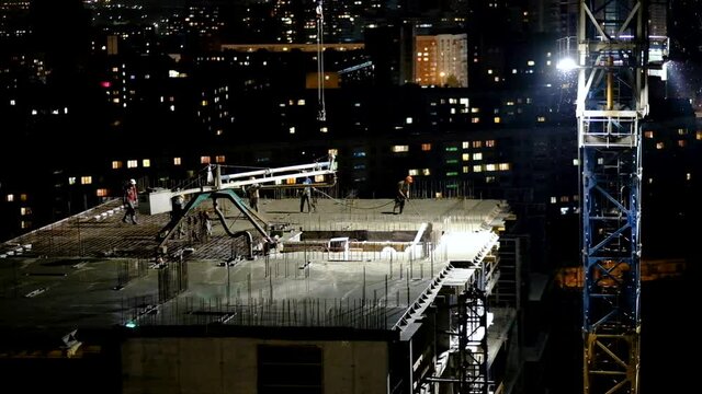 Construction workers pouring wet concrete using concrete spider hose or pump work at high-rise site in night