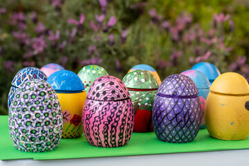 Hand-made Easter eggs on a green pedastal in front of purple lavender flowers.
