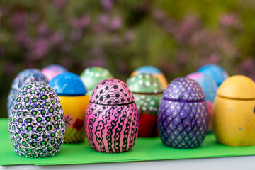 Hand-made Easter eggs on a green pedastal in front of purple lavender flowers.
