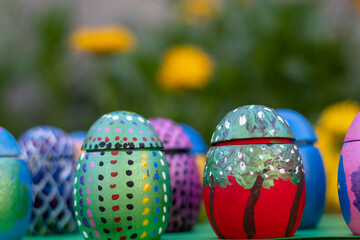 Hand-made Easter eggs on a green pedastal in front of yellow and orange spring flowers
