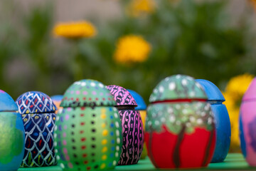 Hand-made Easter eggs on a green pedastal in front of yellow and orange spring flowers