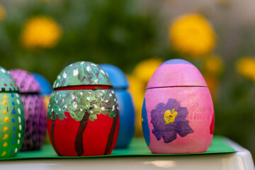 Hand-made Easter eggs on a green pedastal in front of yellow and orange spring flowers