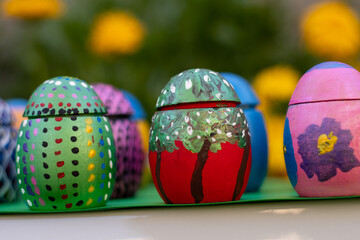 Hand-made Easter eggs on a green pedastal in front of yellow and orange spring flowers