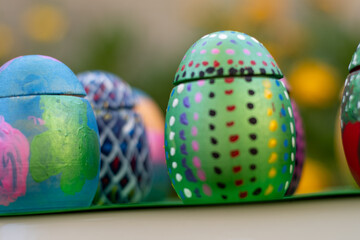 Hand-made Easter eggs on a green pedastal in front of yellow and orange spring flowers