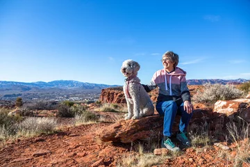 Acrylglasbilder Arizona Happy senior woman on an outdoor hike with her dog. Enjoying nature on a sunny day. Enjoying a scenic overlook in St. George, Utah  © Brocreative