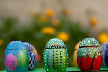 Hand-made Easter eggs on a green pedastal in front of yellow and orange spring flowers