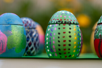 Hand-made Easter eggs on a green pedastal in front of yellow and orange spring flowers