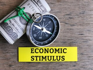 Business and economy concept. Phrase ECONOMIC STIMULUS  written on sticky note with fake money and compass.