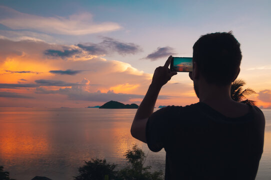 Young man taking a photo of a magnificent sunset at the sea, Koh Phangan, Thailand