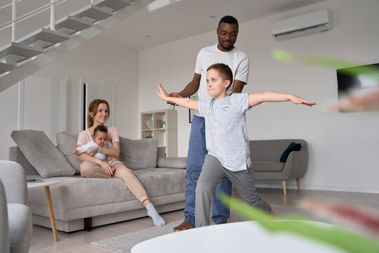 African american young dad teaching caucasian teen son learning doing morning exercises at home. Happy active multiethnic diverse mixed race family with kids having fun spending time at home together