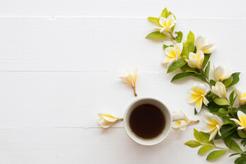 Obraz na płótnie Canvas hot coffee espresso with yellow flowers frangipani arrangement flat lay postcard style on background wooden