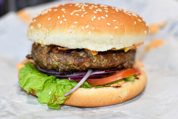 Delicious juicy burger on white wrapping paper background. Cutlet, cheese and vegetables inside fresh sesame bun. delicious street food, fast food, beef burger, close up