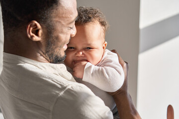Happy tender African American man father holding cute adorable little child daughter enjoying sweet...
