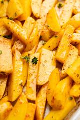 Sliced raw potatoes with spices and herbs on the pan ready for cooking. Selective focus. Shallow depth of field.