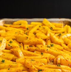 Sliced raw potatoes with spices and herbs on the pan ready for cooking. Selective focus. Shallow depth of field.