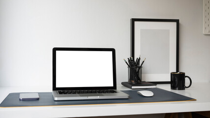 Computer laptop with blank screen, smart phone, pencil holder and empty frame on home office desk.