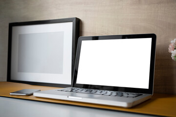 Mock up computer laptop with blank screen, smart phone and empty frame on designer workplace.
