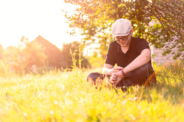 a teenage boy in a cap sits in the tall grass by the bush and looks at his watch. waiting for a meeting. teenage love. summer time in the village