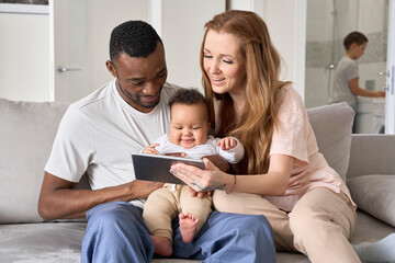 Happy interracial Black and white ethnic family couple enjoying using digital tablet having fun...