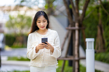 Asian lady using mobile phone for texting message while walking along the modern resident in urban...