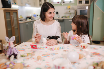 Fototapeta premium Little girl with her mom preparing for easter and print eggs. They are sitting by the table and have fun