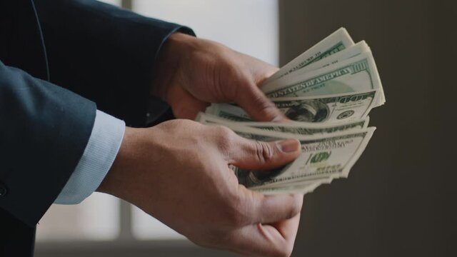 Cropped view unrecognizable successful caucasian business man with pile of dollars banknotes counting money in office. Close up male hands counts salary bank payments. Concept of financial profit