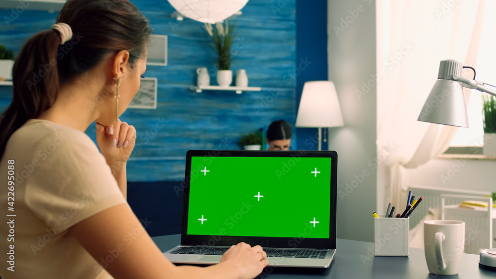 Poster freelancer looking at laptop computer with mock up green screen chroma key display sitting on desk t
