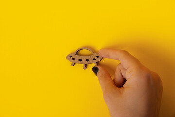 wooden symbol UFO in hand over yellow background
