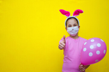 A girl in a pink T-shirt and rabbit ears on a yellow background in her hands holds a balloon and shows a finger class, cool, place for advertising. 