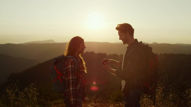 Hikers enjoying hike in mountains at sunset. Man proposing marriage to woman 