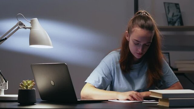 Night study. Creative block. Hard task. Stress frustration. Annoyed angry tired female student writing essay dissatisfied creasing paper throwing away at home workplace with laptop textbooks.