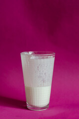Half-empty glass of kefir on a pink surface with shadows.